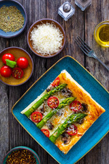 Baked puff pastry, green asparagus with mozzarella cheese, mushrooms and cherry tomatoes on wooden table
