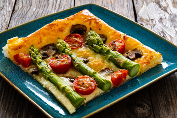 Baked puff pastry, green asparagus with mozzarella cheese, mushrooms and cherry tomatoes on wooden table
