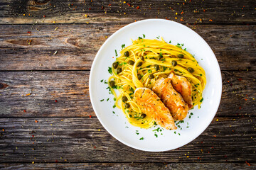 Chicken piccata with spaghetti and capers in sauce on wooden background
