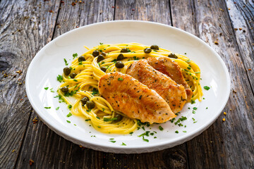 Chicken piccata with spaghetti and capers in sauce on wooden background
