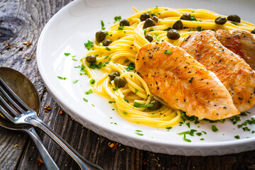 Chicken piccata with spaghetti and capers in sauce on wooden background
 - obrazy, fototapety, plakaty