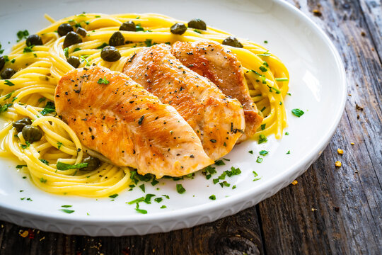 Chicken piccata with spaghetti and capers in sauce on wooden background
