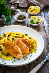 Chicken piccata with spaghetti and capers in sauce on wooden background
