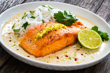 Creamy coconut lime salmon with rice noodles on wooden table