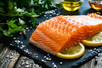 Fresh raw salmon steak with salt and fresh vegetables on black stone plate
