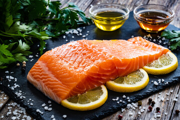 Fresh raw salmon steak with salt and fresh vegetables on black stone plate
