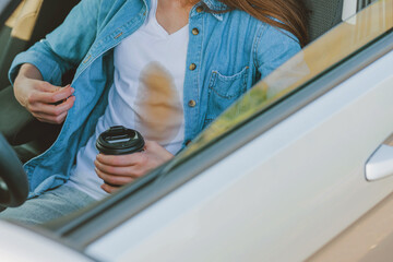 A faceless girl spilling coffee or tea on herself while driving a car. Spoiled clothes. Concept of cleaning stains on clothes.