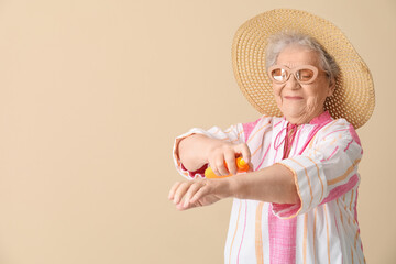Senior woman applying sunscreen cream on beige background