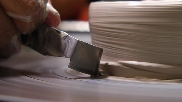 A potter is working a clay cup on a potter's wheel with a special tool. A close-up view. A potter is practicing pottery, handicraft, working with clay