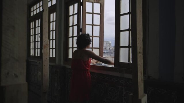 Young woman opening window and looking the city from old abandoned loft - Dreams and inspiration 