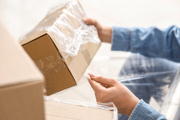 Young woman wrapping cardboard box with stretch film at home on moving day, closeup