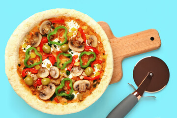 Board with vegetable pizza and cutter on blue background