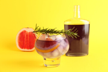 Glass of purple gin and tonic with bottle, grapefruit and rosemary on yellow background
