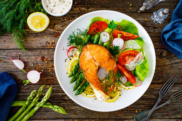 Seared salmon steak with fried green asparagus and fresh vegetable salad served on wooden table
