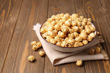 Bowl with crispy popcorn on wooden background