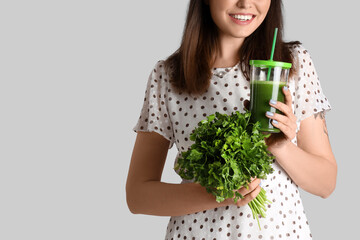 Young woman with glass of vegetable juice and parsley on grey background, closeup