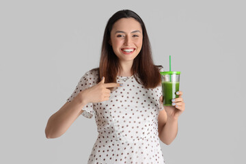 Young woman pointing at glass of vegetable juice on grey background