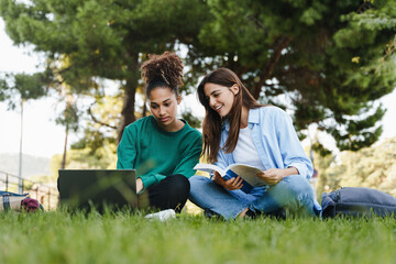 Naklejka na ściany i meble Two female students working and learning together for exams sitting on University campus grass