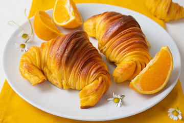 Freshly baked portuguese Brioche croissants on a plate with oranges. Close-up