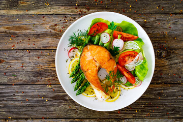 Seared salmon steak with fried green asparagus and fresh vegetable salad served on wooden table
