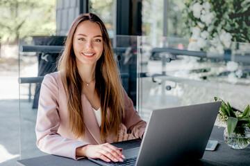 Young woman working remotely from a cafe, using laptop, smiling