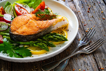 Seared salmon steak with fried green asparagus and fresh vegetable salad served on wooden table
