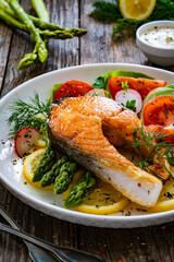 Seared salmon steak with fried green asparagus and fresh vegetable salad served on wooden table
