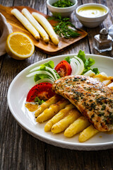 Seared chicken breast with white cooked asparagus and fresh vegetables on wooden table
