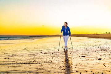 Nordic walking - woman training on beach at sunset

