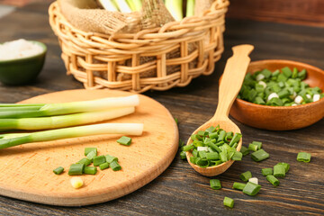 Board and spoon with fresh green onion on wooden background