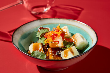 Eggplant-tofu salad in a ceramic bowl, Asian style, set against a dark red velvet backdrop, wine glass in the background