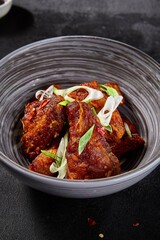 Vertical side view of buffalo wings in Asian style on a black background. Decorated with sliced greens, spices, and chopsticks