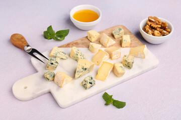 Board with pieces of tasty cheese on light background