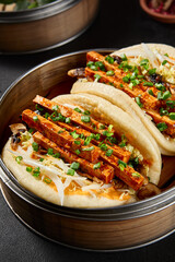 Vertical side view of bao buns with tofu and vegetables in a steamer on a black background