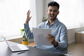Angry concerned Indian business leader man holding legal document, sales report, paper letter, reading bad news, having problems, financial mistake, loss, bank rejection