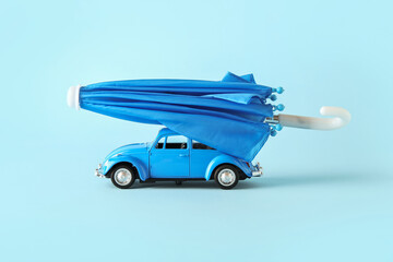 Creative composition with toy car and mini umbrella on blue background. Insurance concept