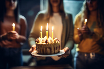 unrecognizable Young woman holding a birthday cake in a bar, She is ready to blow the candles, Her friends standing in back at bar counter and they are defocused