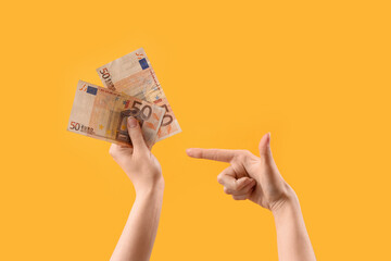 Woman pointing at euro banknotes on yellow background