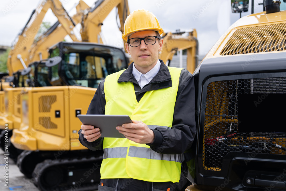 Aufkleber engineer in a helmet with a digital tablet stands next to construction excavators