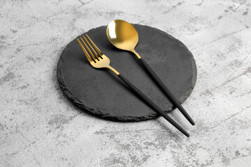 Board with golden spoon and fork on grey background
