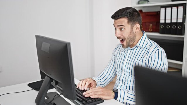 Young hispanic man business worker using computer working with winner expression at office
