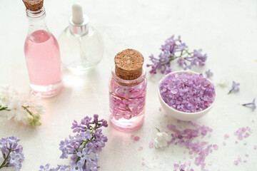Obraz na płótnie Canvas Bottles of cosmetic oil with beautiful lilac flowers and sea salt on white table