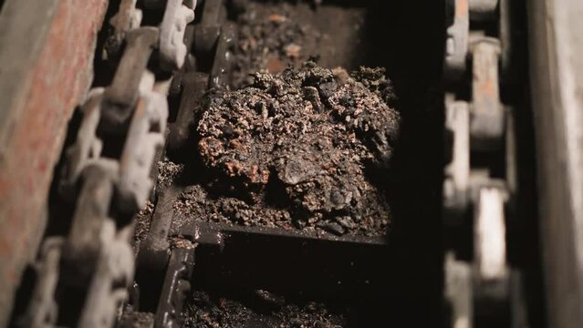 Transporting wet coal slag with automatic chain conveyor closeup. Used fossil fuel leftovers removing from heating furnace in industrial factory workshop