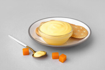 Plate with bowl of tasty cheddar cheese sauce and crackers on grey background