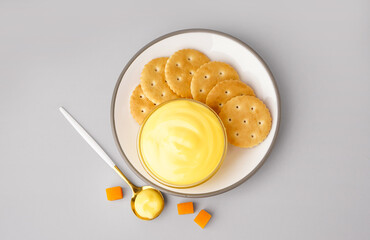 Plate with bowl of tasty cheddar cheese sauce and crackers on grey background
