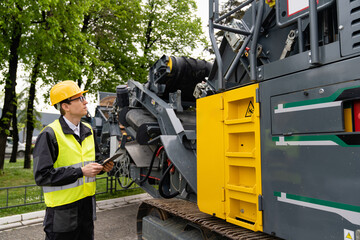 Engineer with digital tablet next to road construction machine.