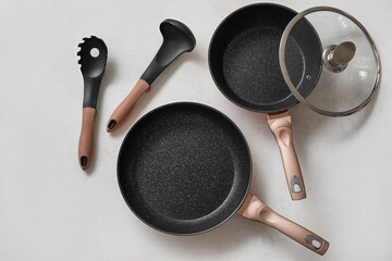 Frying pans and kitchen utensils on light background - obrazy, fototapety, plakaty