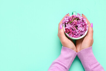 Female hands holding cup with lilac flowers on turquoise background