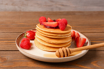Plate with sweet pancakes and berries on wooden table, closeup