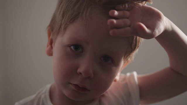 Powerless little boy wipes sweat with hand from forehead on beige background. Tired chubby toddler takes break from workout in gym closeup slow motion